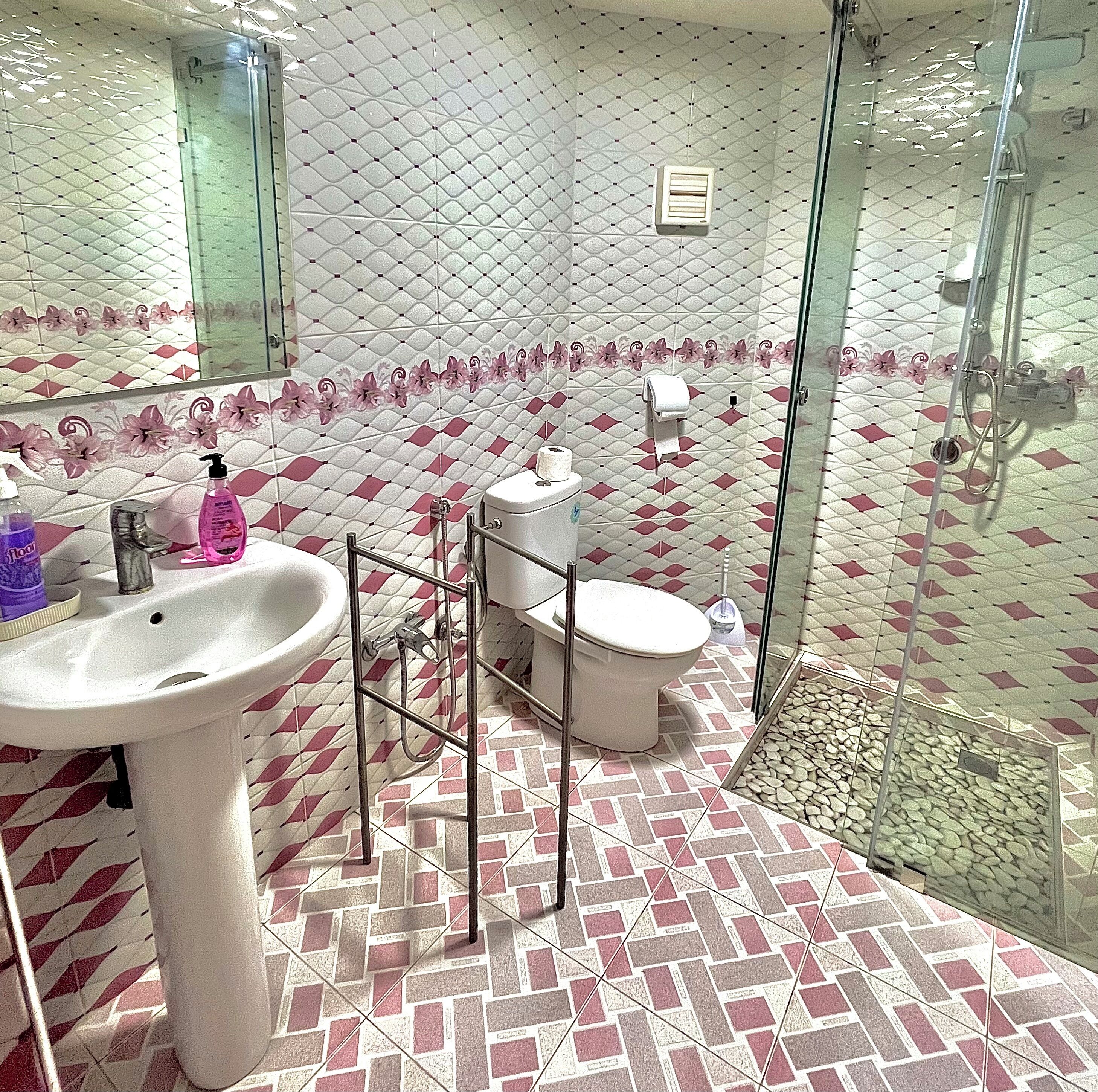 Un baño con piso estampado, un lavamanos, un inodoro y una cabina de ducha de vidrio.