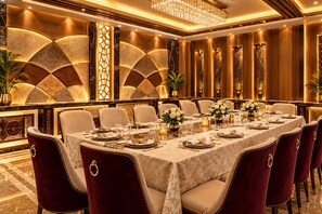 A formal dining room with a long table set for a meal, surrounded by plush chairs. - The Narayanam Hotel (Gwalior)