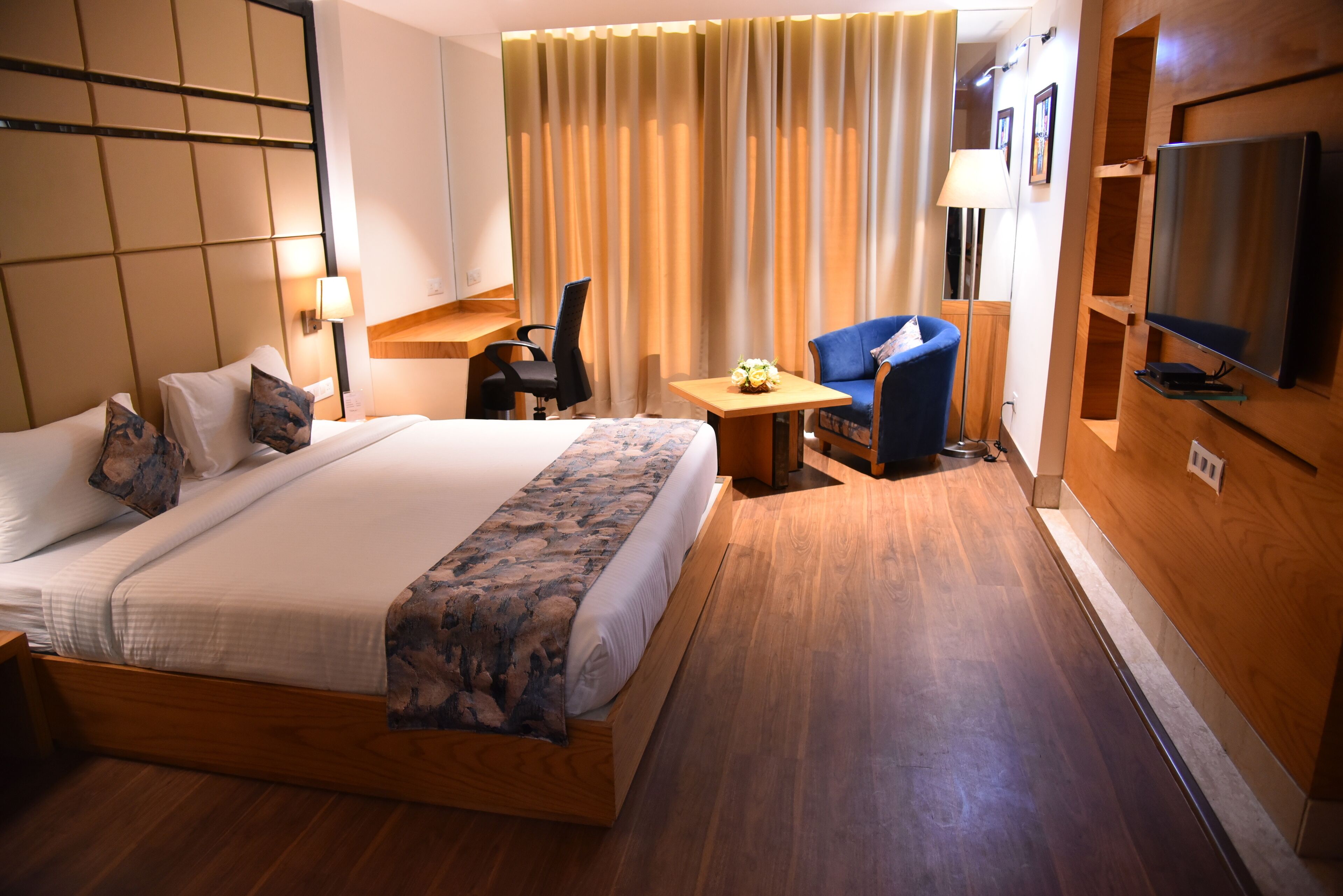 A hotel room with a large bed, a desk, a chair, a TV, and a curtain.