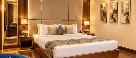 A modern hotel bedroom with a large bed, bedside tables, a mirror, and artwork on the wall.