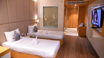 A hotel room with two beds, a TV, a window, and a wooden floor.