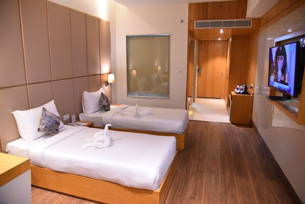 A hotel room with two beds, a TV, a window, and a wooden floor. - The Narayanam Hotel (Gwalior)