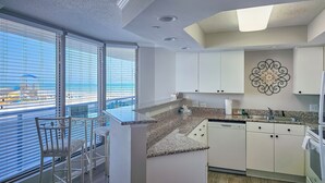 A modern kitchen with white cabinets, granite countertops, and a view of the beach through large windows. - Brighton 103, ocean view condo, access to all resort amenities. (Myrtle Beach)