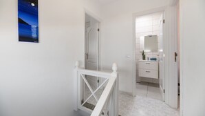 A hallway with a white railing, a door leading to a bathroom, and a framed picture on the wall.