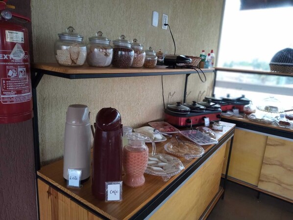 A café counter with various food items, a fire extinguisher, and a coffee machine. - Pousada Ohana (Tamandaré)