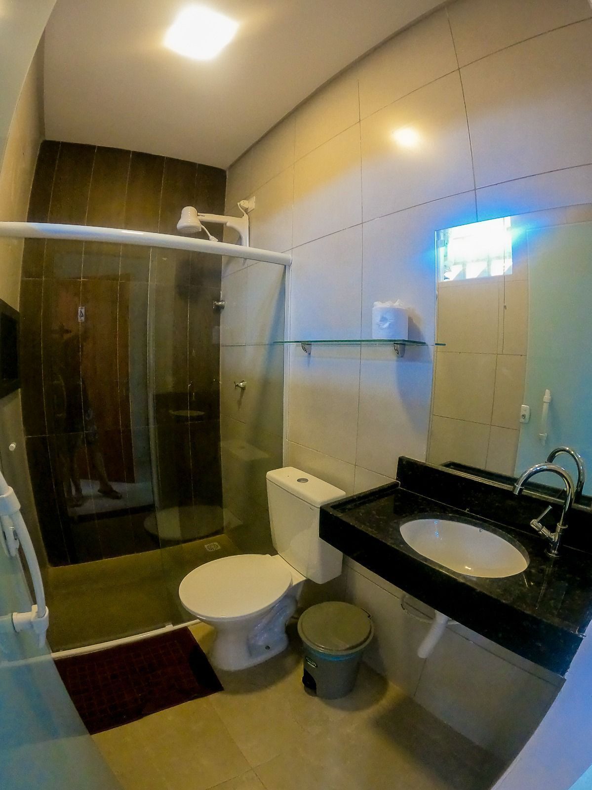 A modern bathroom with a glass shower enclosure, a toilet, a sink, and a small trash bin.