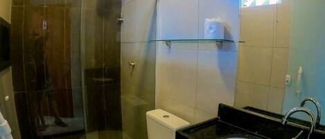 A modern bathroom with a glass shower enclosure, a toilet, a sink, and a small trash bin.