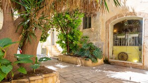 A courtyard with a palm tree, potted plants, and a window with a decorative wheel. - La Casa di Nonna Anna by Wonderful Italy (Siracusa)