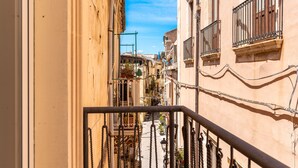 A narrow street with buildings on either side, featuring balconies with wrought iron railings and a clear blue sky above. - La Casa di Nonna Anna by Wonderful Italy (Siracusa)