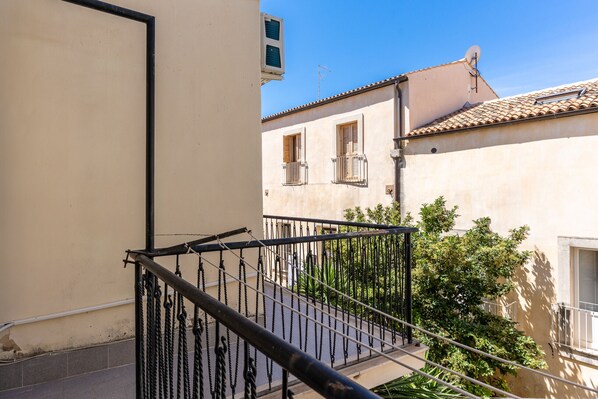 A balcony with a metal railing overlooking a courtyard with a building in the background.