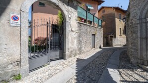 A narrow cobblestone street with stone buildings, a metal gate, and a sign indicating a no parking area.