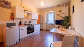 A modern kitchen with white cabinets, a microwave, and a stove. There's a dining table with a chair and a potted plant.