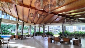 A spacious indoor area with wooden ceiling beams, hanging geometric-patterned lamps, and a view of a pool and greenery outside. - Verdon Parc Davao City by darpm (Davao)