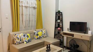 Un salon comprenant un canapé, une table basse, un téléviseur et une petite étagère ornée d’objets décoratifs.