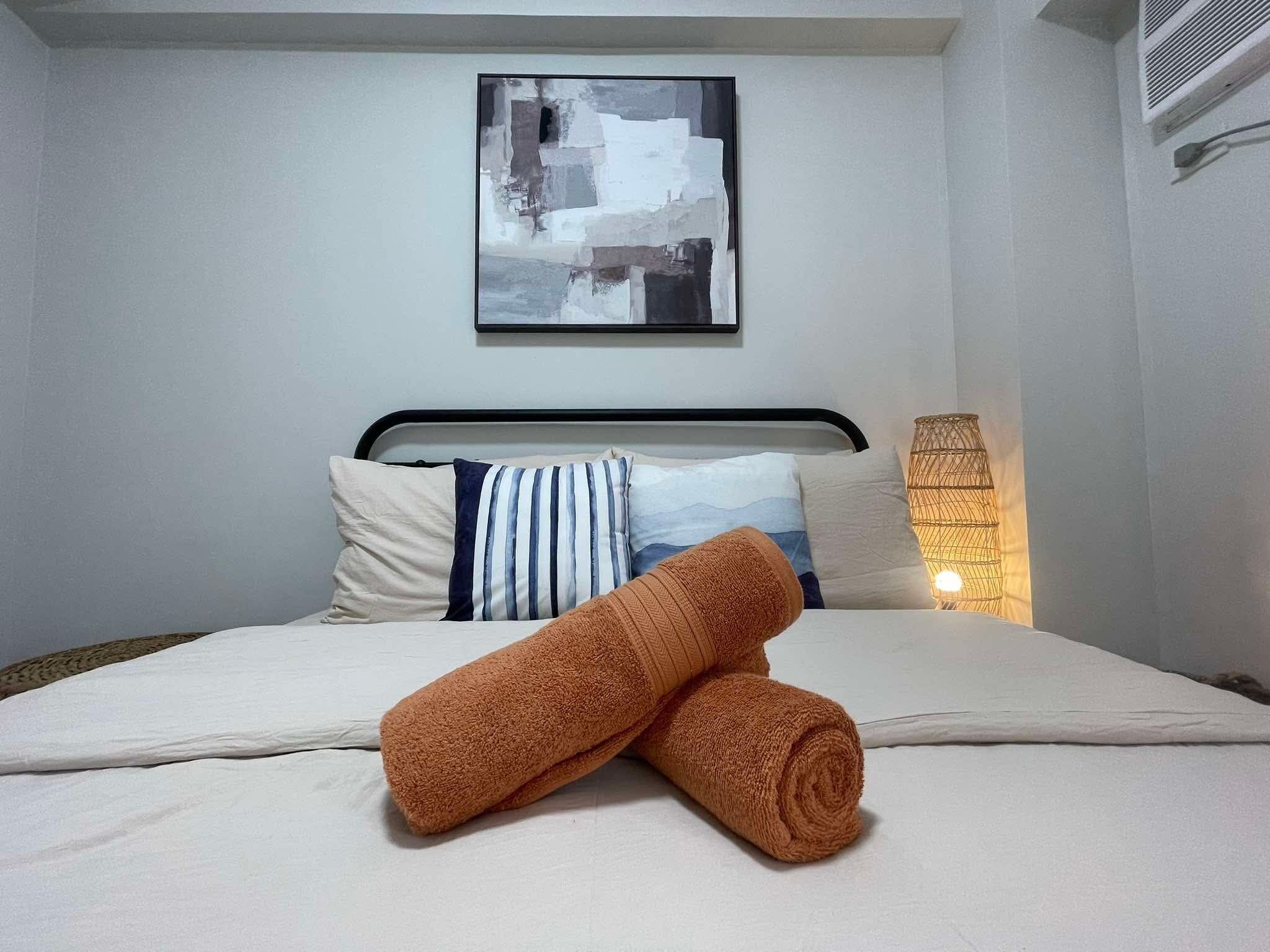 Una cama bien hecha con edredón blanco, dos almohadas y una toalla marrón enrollada.