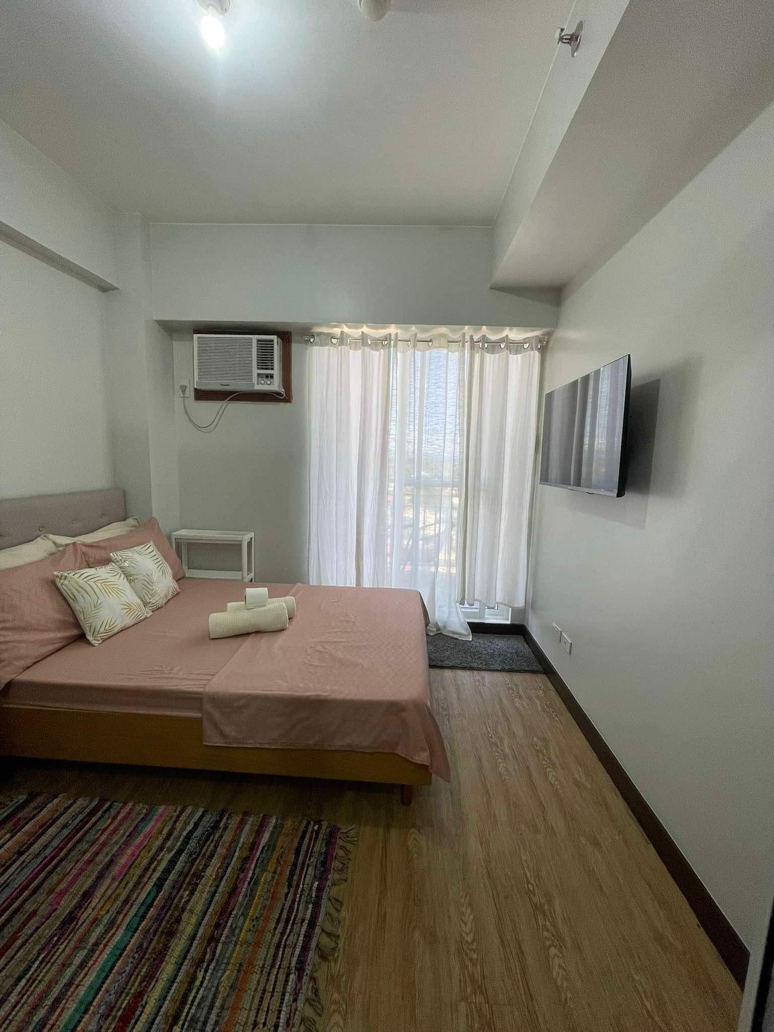 A bedroom with a bed, a TV, an air conditioner, and a window with curtains.