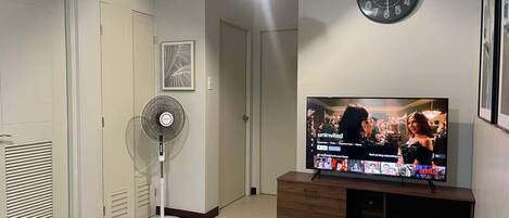 Una sala de estar con televisión, un reloj, un ventilador y una puerta.