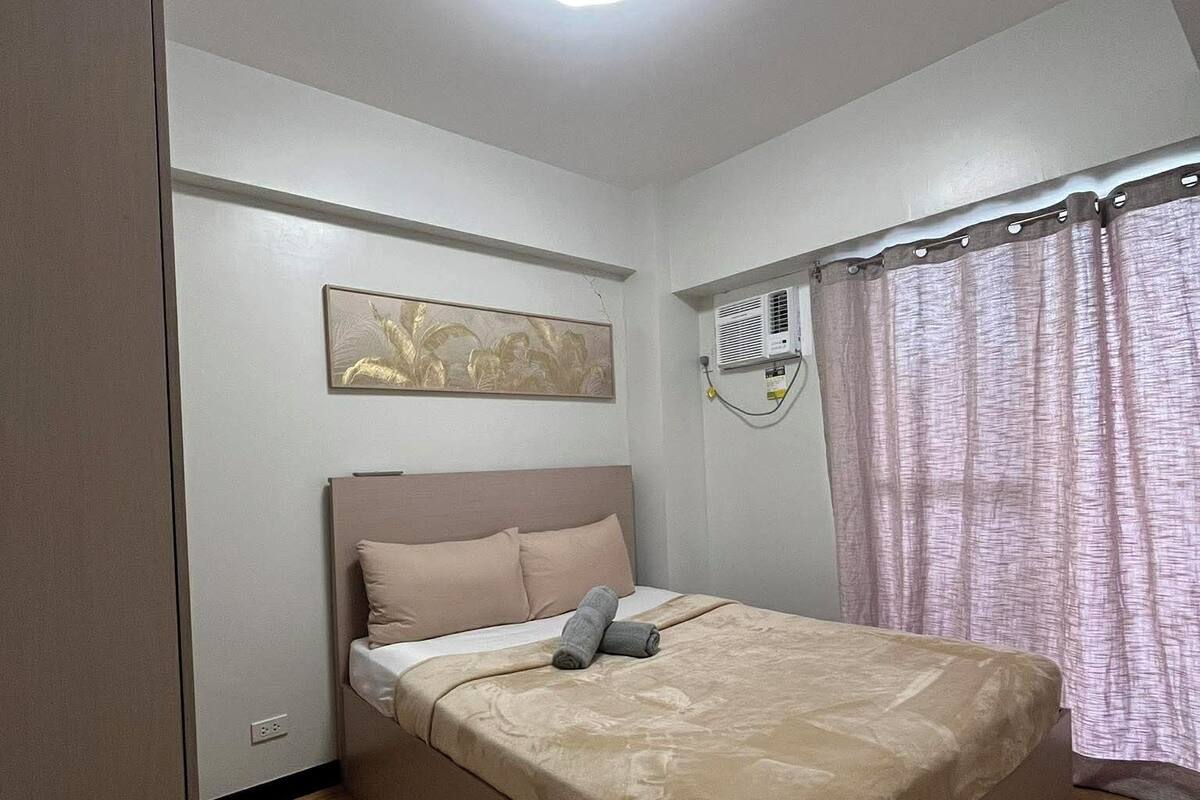 Ein Schlafzimmer mit einem Einzelbett, einer Deckenleuchte, einer Klimaanlage, einem Fenster mit Vorhängen und einer Wand-Klimaanlage.
