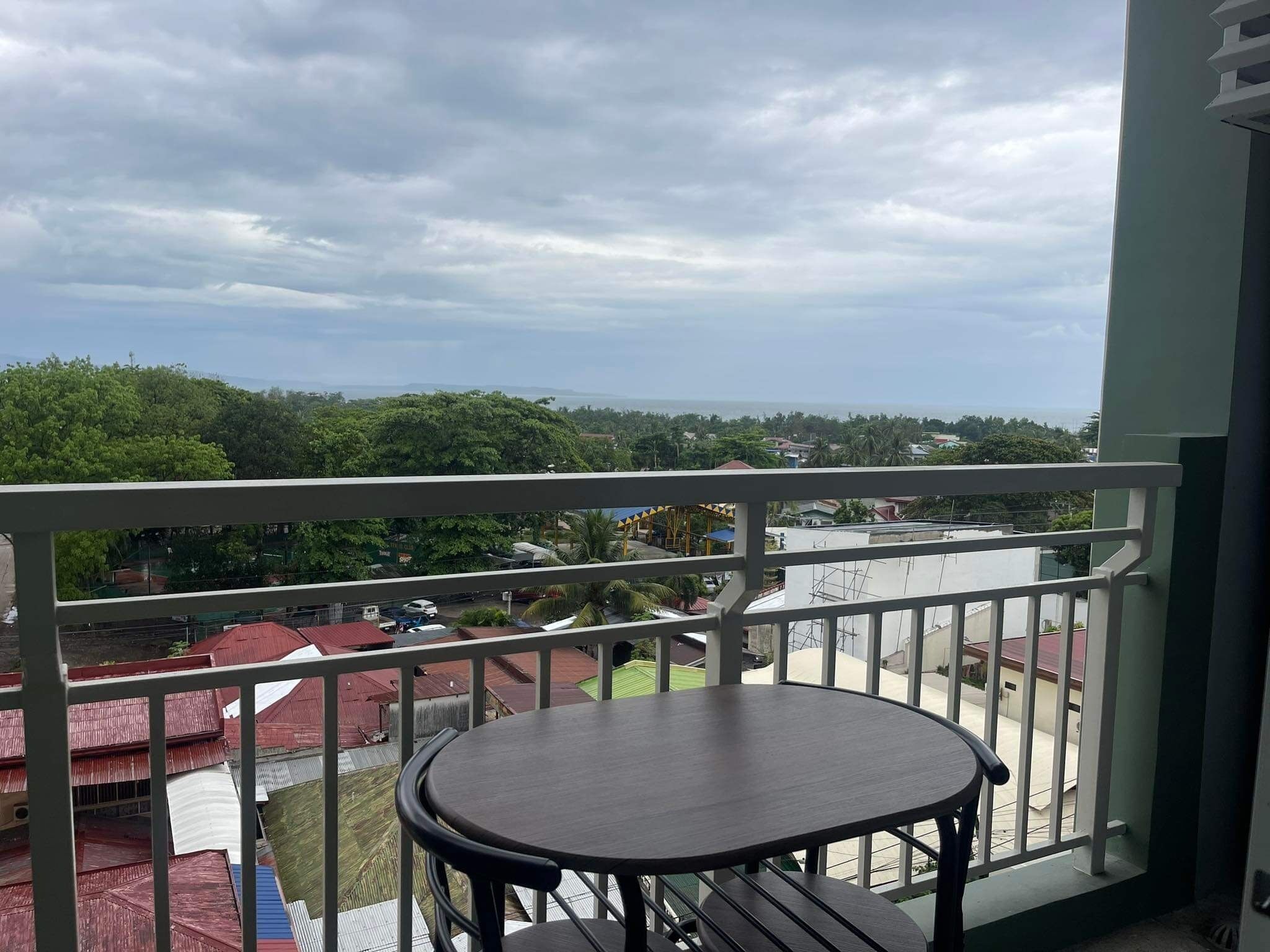 A balcony with a round table and chairs, overlooking a residential area with houses and greenery.