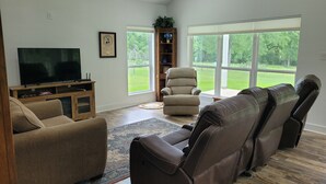 A living room with a large flat-screen TV, a beige sofa, a brown leather recliner, and a wooden entertainment unit. - Country living in new 2bdrm/2bth farmhouse in lovely Chappell Hill with WiFi, AC (Chappell Hill)