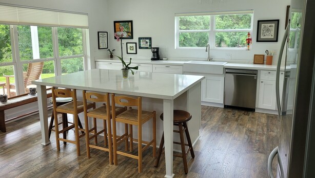 A modern kitchen with a large island, wooden chairs, and a view of the outdoors through large windows. - Country living in new 2bdrm/2bth farmhouse in lovely Chappell Hill with WiFi, AC (Chappell Hill)