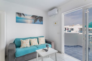A living room with a sofa, a coffee table, and a painting of a beach scene. - Sueño Del Mar Vacation Apartment with Shared Pool, Wi-Fi & Air Conditioning (Puerto del Carmen)