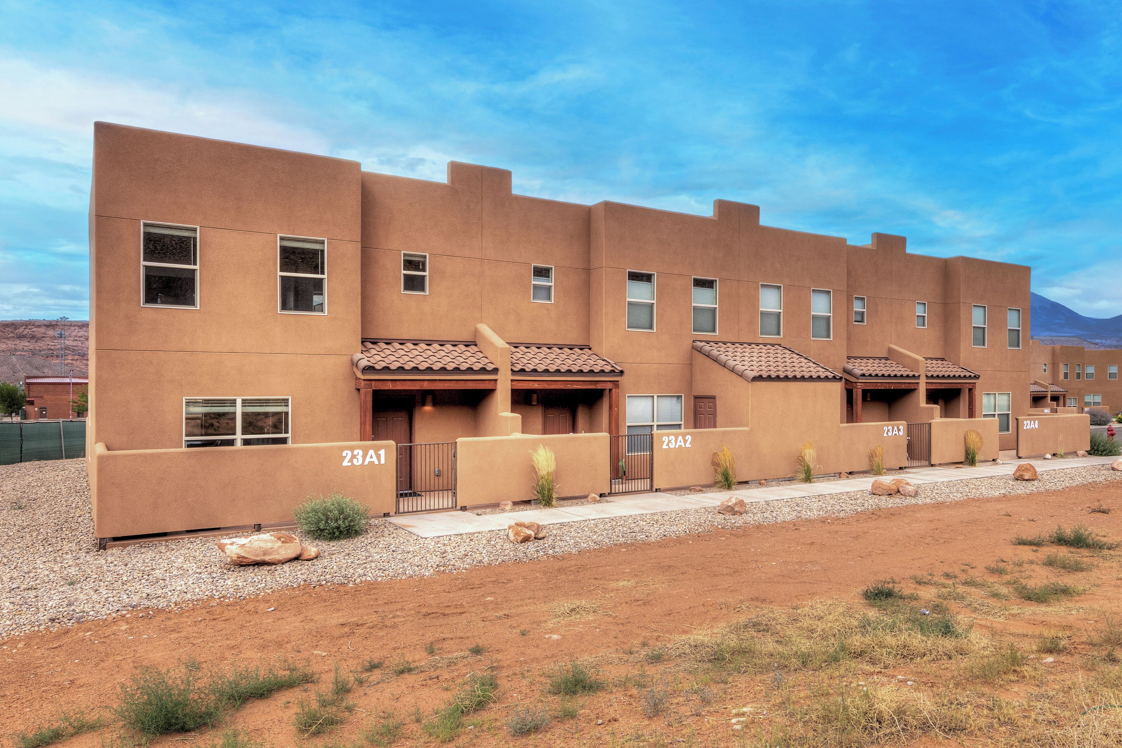 A multi-story building with numbered units, a gravel driveway, and a clear sky.