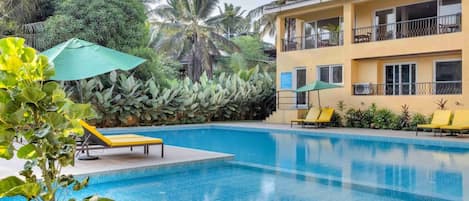 Una piscina con sillas de descanso y un edificio con balcones.