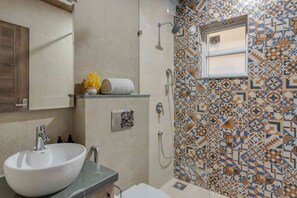 A bathroom with a large white sink, a shower with a handheld showerhead, and a tiled wall with geometric patterns. - 1bhk w Balcony and Pool - 5 Mins to Candolim Beach (Candolim)