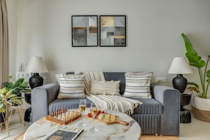A modern living room with a grey sofa, striped cushions, a chessboard, wine glasses, and a coffee table. - Cozy 1bhk w Balcony nr Candolim Beach Vp-b210 (Candolim)