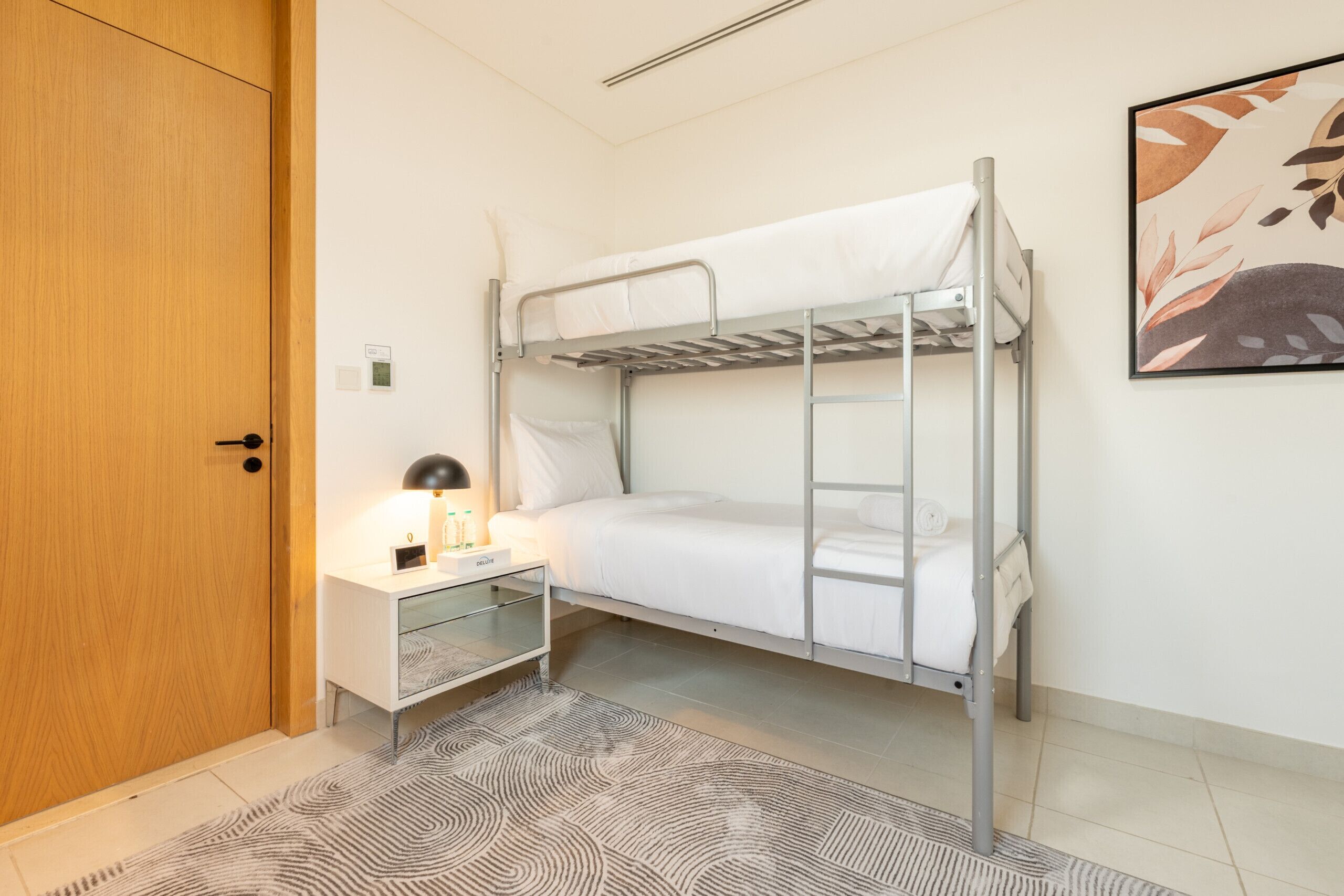 Une chambre avec un lit superposé, une table de chevet, une lampe et un tableau encadré au mur.