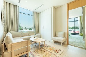 Een moderne woonkamer met een bank, een salontafel en een fauteuil. Een groot raam biedt uitzicht op de omgeving.