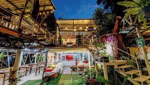 Un espace de restauration en plein air avec plusieurs tables et chaises, un grand vase décoratif et un escalier menant à un niveau supérieur.