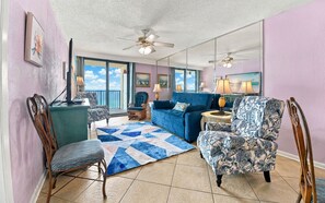 Un salon avec un canapé bleu, un fauteuil à motifs et une vue sur l’océan par de grandes fenêtres.