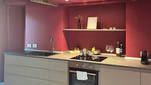 Una cocina moderna con una pared roja decorativa, vigas de madera, horno empotrado y una encimera con diversos objetos.