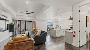 A modern kitchen with white cabinets, a central island, and a dining area with a grey sofa and brown armchair. - Desert Jewel With Private Gym And Pool 4 Bedroom Townhouse (Hurricane)