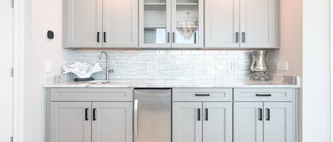 A modern kitchen with light grey cabinets, a stainless steel dishwasher, and a white tiled backsplash.