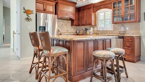 Una cocina con armarios de madera, un refrigerador de acero inoxidable y una isla grande con taburetes de bar.