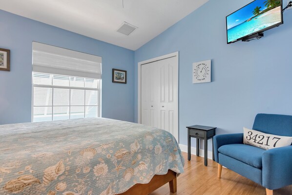 A bedroom with a bed, a blue armchair, a television on the wall, and a door.