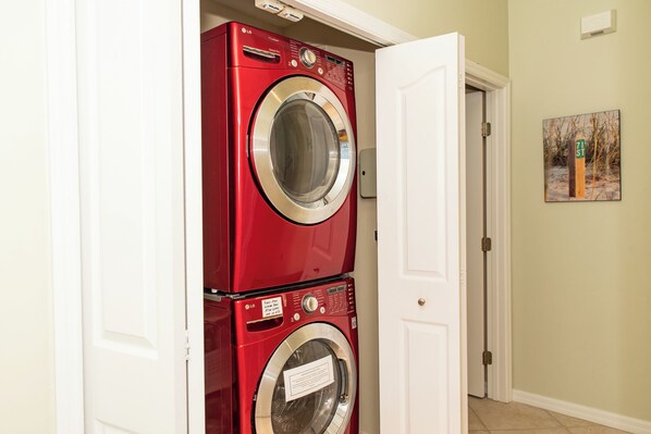 A red stacked washer and dryer in a hallway with a white door and a small picture on the wall.