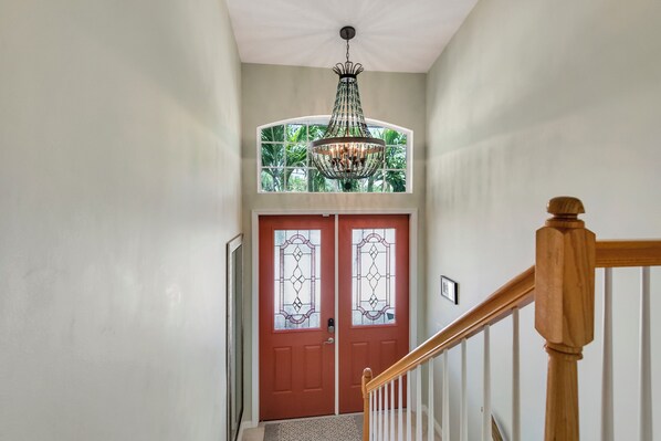 Un pasillo con una puerta roja, un candelabro y una escalera de madera.
