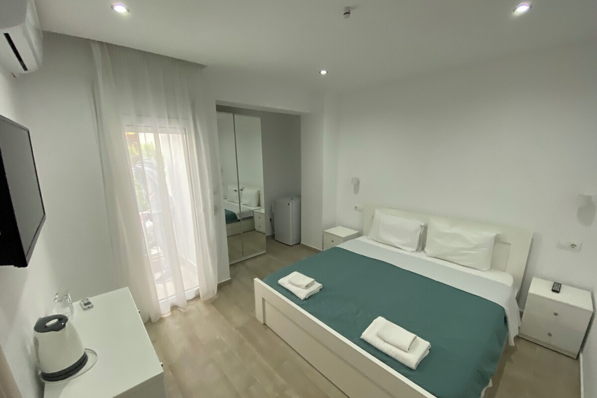 A hotel room with a bed, a bedside table, a mirror, and a window with curtains.