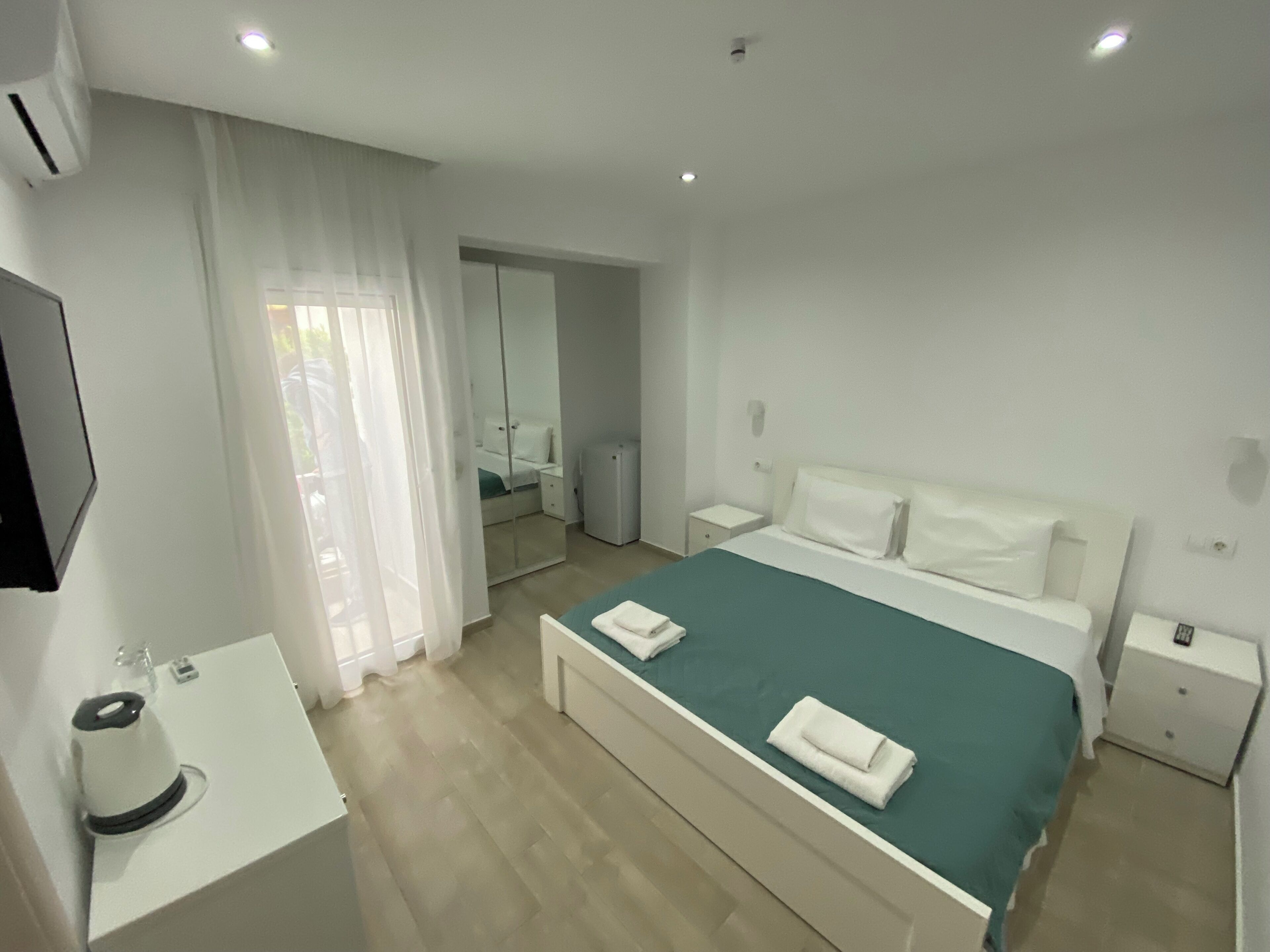 A hotel room with a bed, a bedside table, a mirror, and a window with curtains.