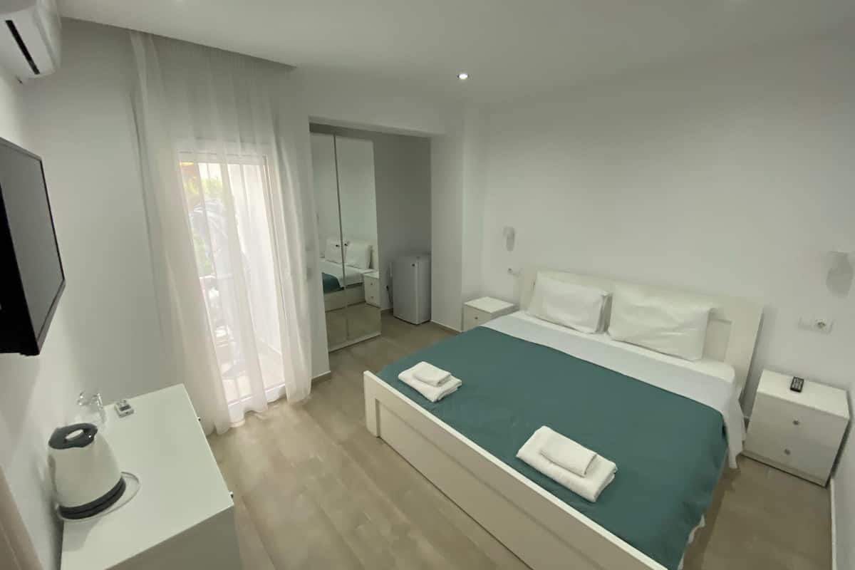 A hotel room with a bed, a bedside table, a mirror, and a window with curtains.