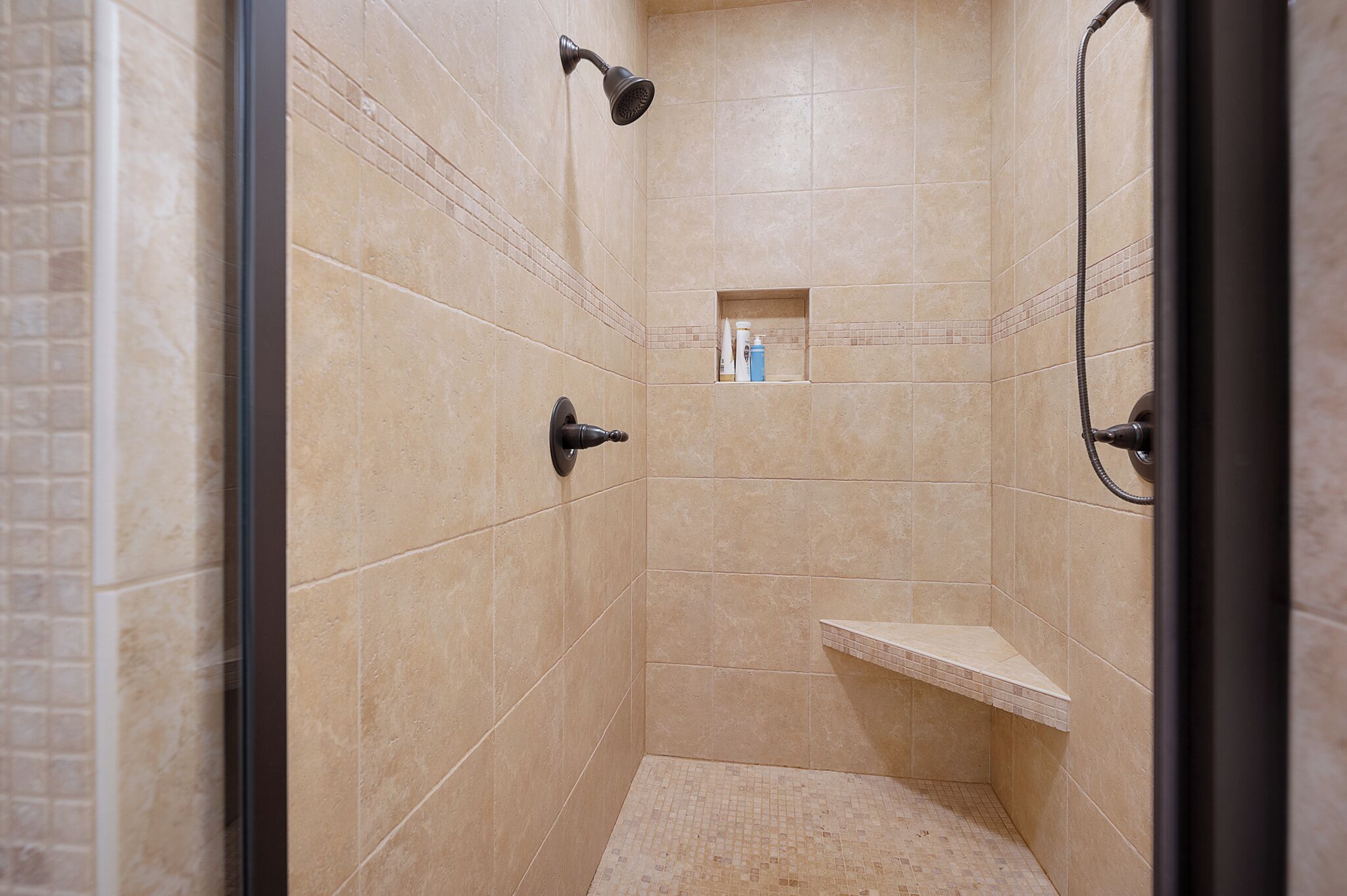 A small, tiled shower with a handheld showerhead and a wall-mounted faucet.