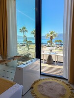 Une chambre d’hôtel avec un lit, un fauteuil massant, une petite table et une vue sur la mer et les palmiers.