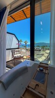 Une pièce baignée de lumière, avec vue sur la mer, comprenant un fauteuil confortable, une petite table et un banc en bois.