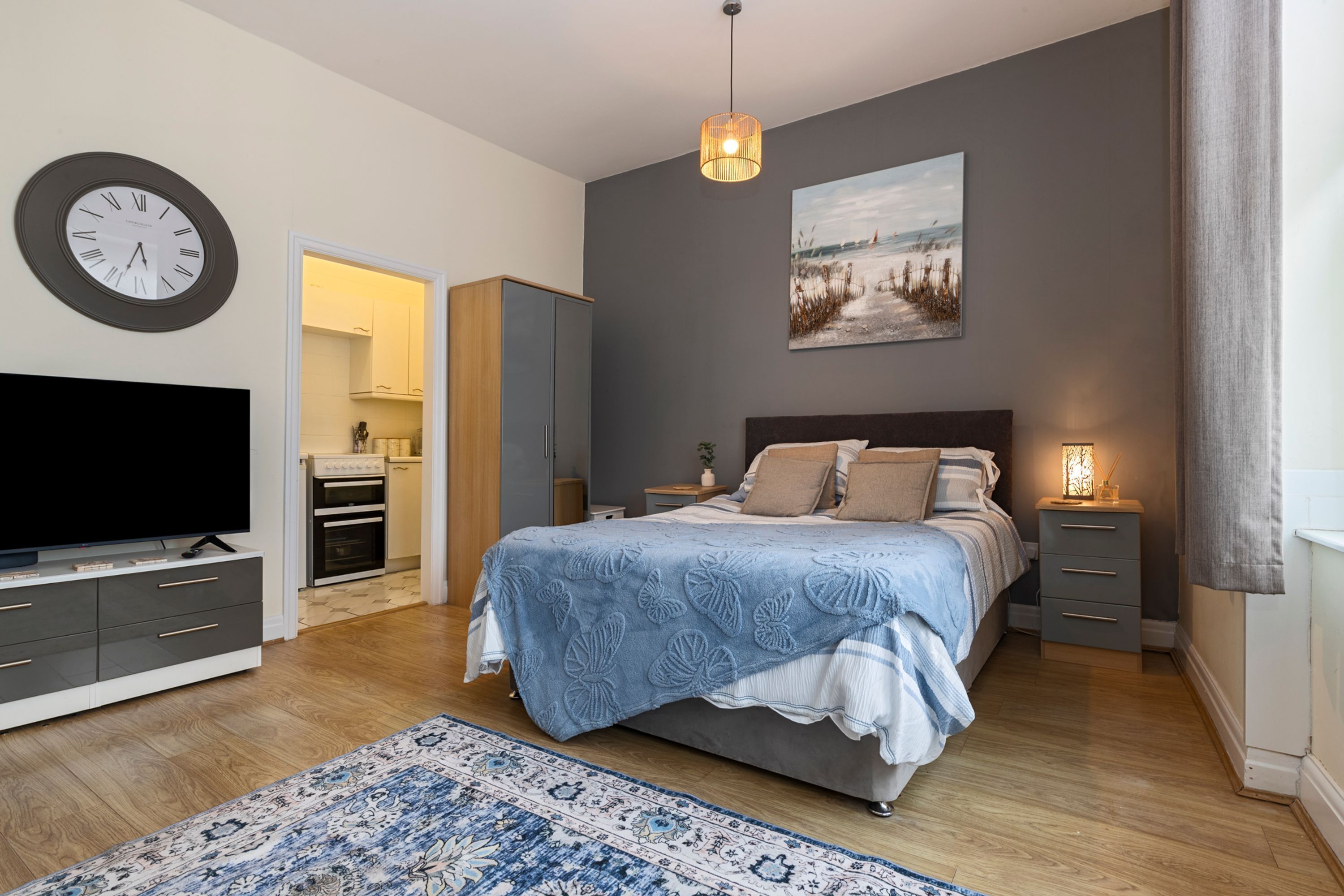 A modern bedroom with a large bed, bedside tables, a TV, a clock, and a painting on the wall.