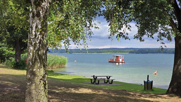 A lakeside park with picnic tables, a boat, and swimmers. - Cozy half of the house near the lake with barbecue, within walking distance of the bathing area & Satama (Wendisch Rietz)