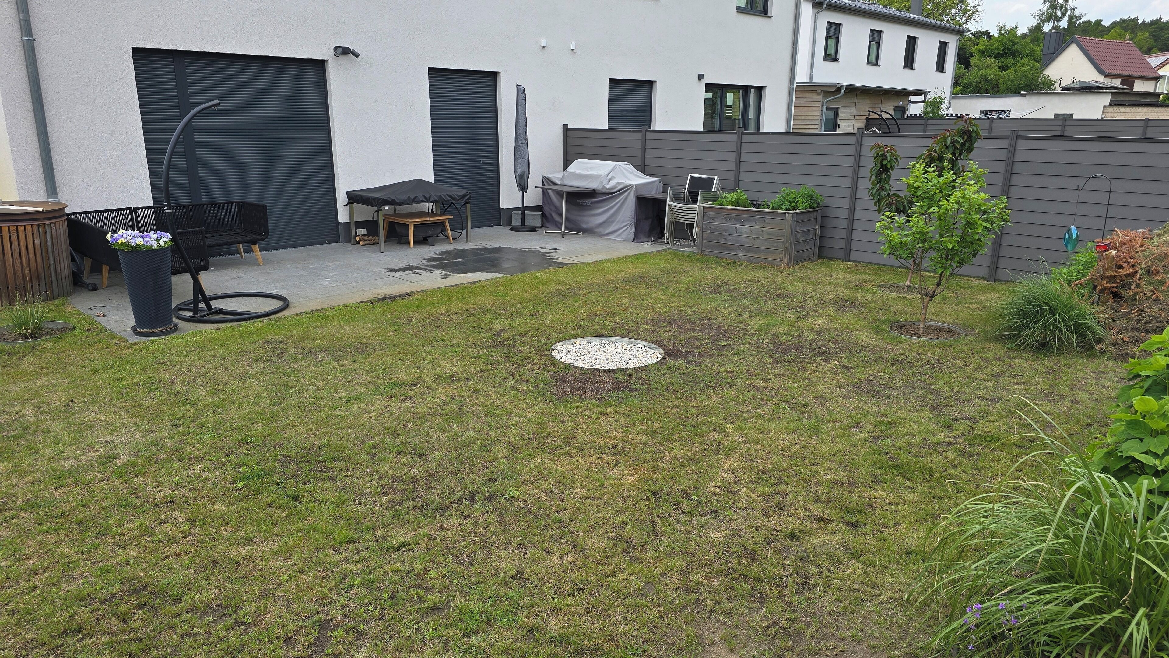A backyard with a lawn, a manhole cover, a barbecue grill, and a covered table.